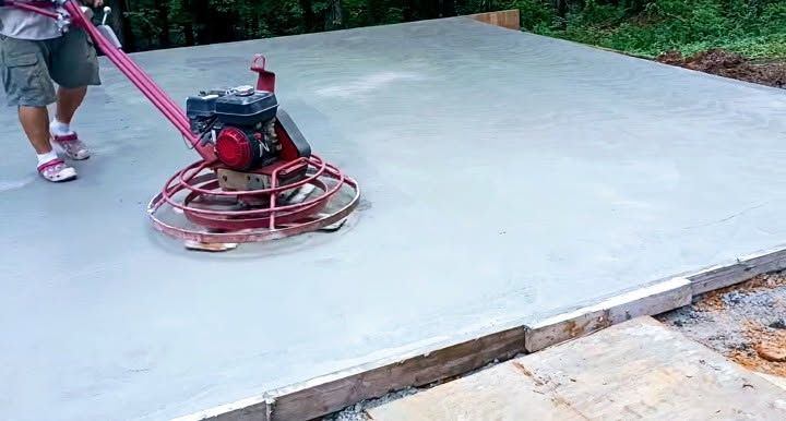 Worker smoothing fresh concrete with a power trowel on a new slab outdoors