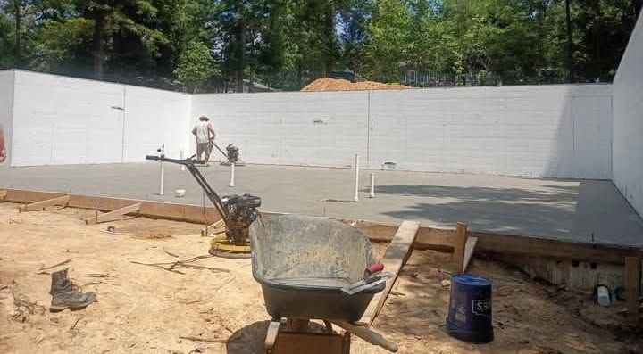 Outdoor construction site with a partially built cinder block wall, wheelbarrow, and tools in the foreground