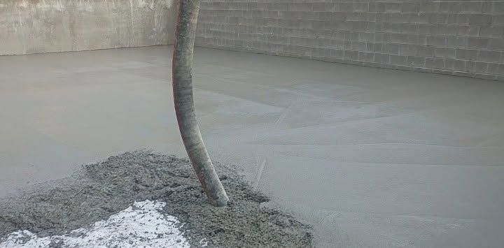 Gray concrete being poured around a bent metal pipe in a construction area.