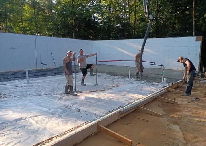 Workers smoothing fresh concrete for a large slab foundation outdoors.