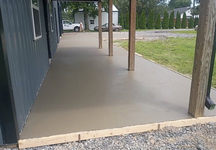 Covered concrete porch beside a dark building, with wooden posts and gravel along the edge.
