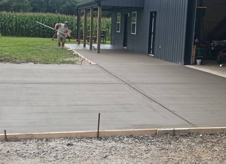 Concrete walkway beside a dark building, with a person mowing grass near the porch.