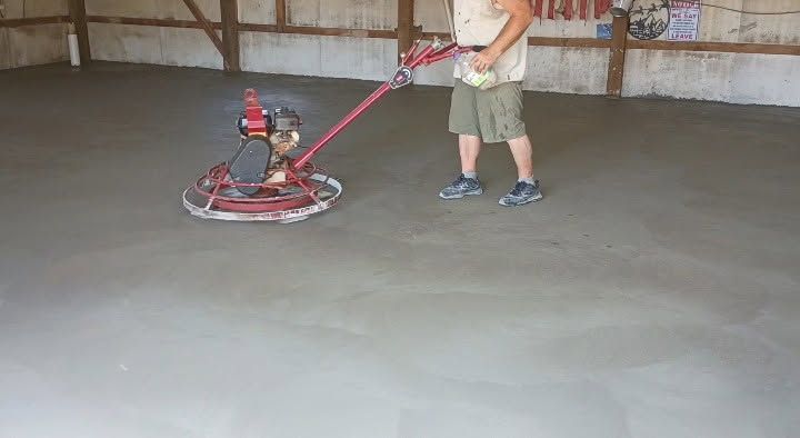 Person using a red floor buffer in an empty garage with a smooth concrete floor