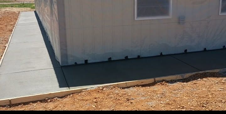 Concrete sidewalk next to a tan building with a small window and dirt ground beside it