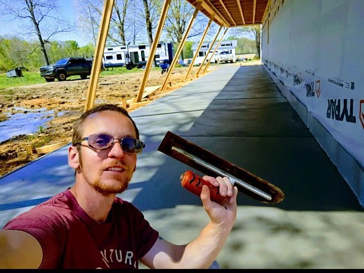 Person holding a long object in a covered outdoor walkway beside a white building, with trucks in the background