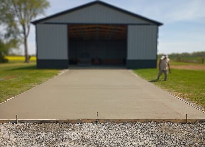 Concrete driveway leading to a large open barn, with a person standing on the right side.