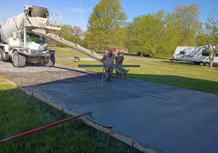 Cement truck pouring a concrete driveway slab while two workers level it in a suburban yard.