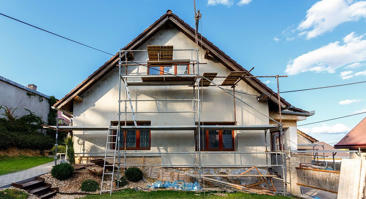 House exterior with scaffolding under construction, white walls and brown roof under a blue sky