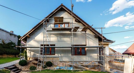 House exterior with scaffolding under construction, white walls and brown roof under a blue sky