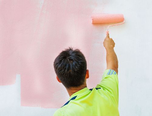 Person painting a wall pink with a roller