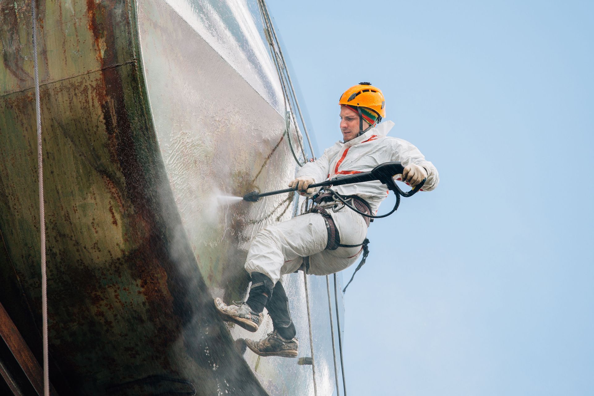 Worker in safety gear rappelling down a building exterior while pressure washing the facade