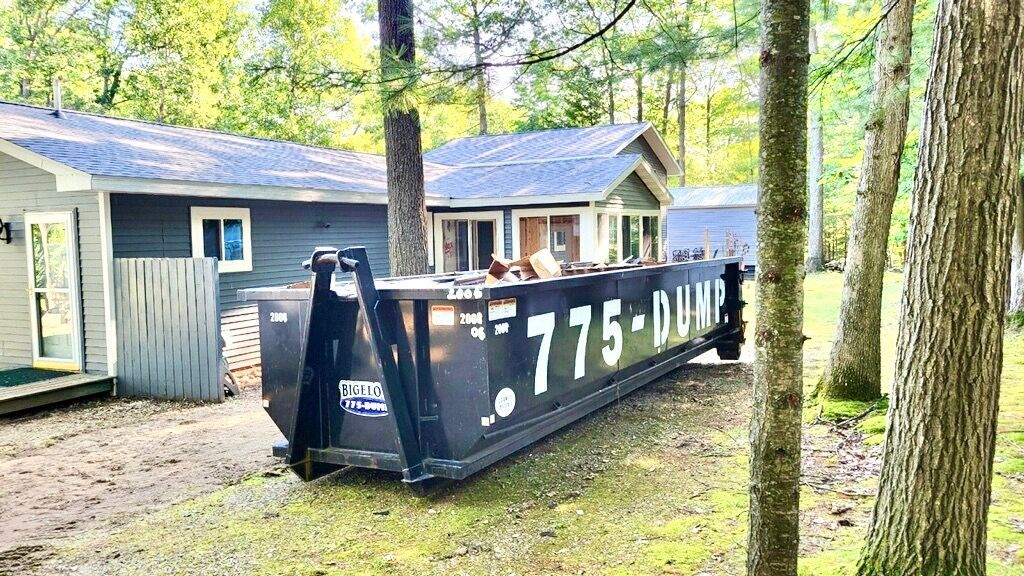 A dumpster is parked in front of a house in the woods