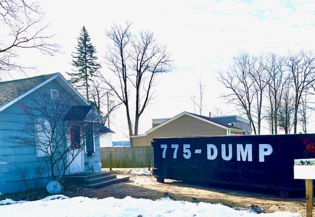 A dumpster is parked in front of a house in the snow