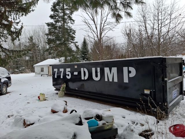 A black dumpster is sitting in the snow in front of a house