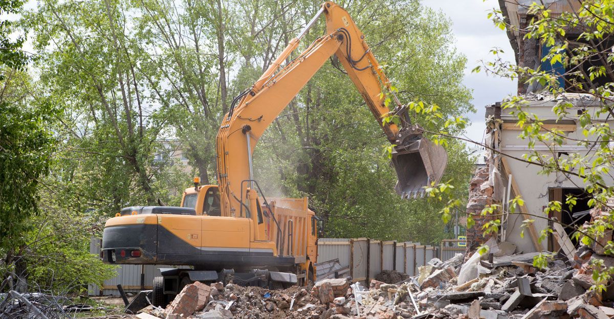 A large yellow excavator is demolishing a building.