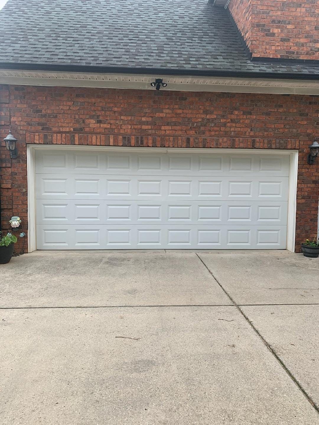 A white garage door is sitting in front of a brick house.