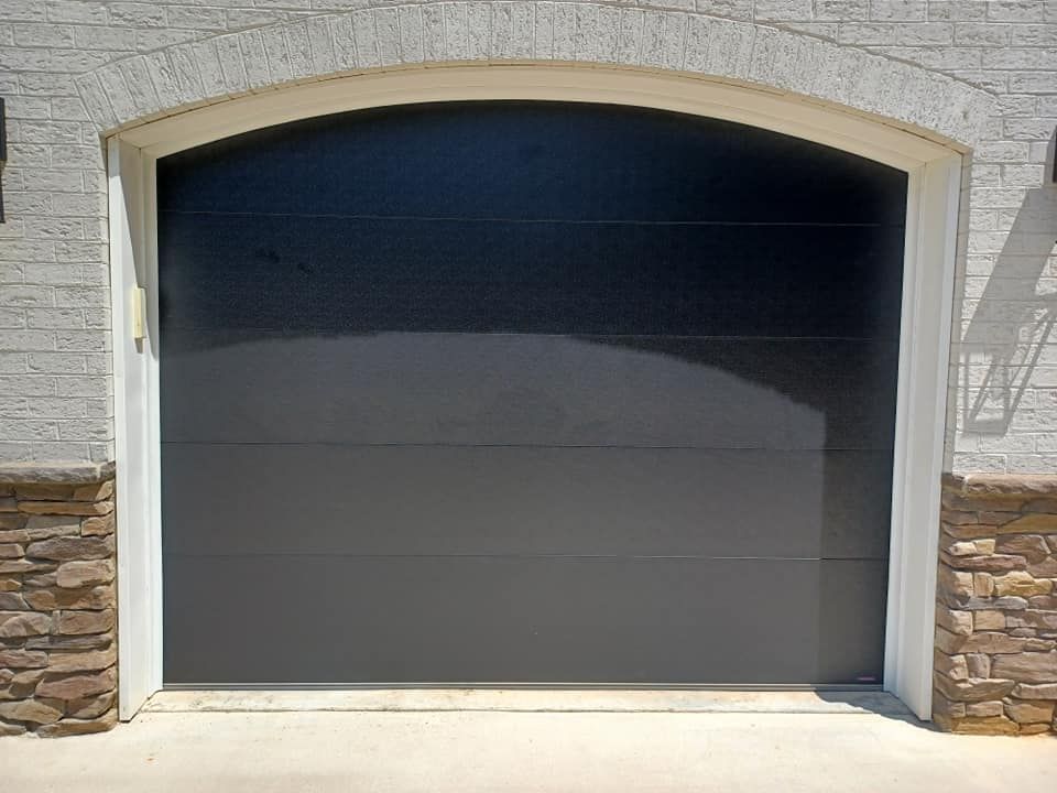A black garage door with a white arch on a white brick building
