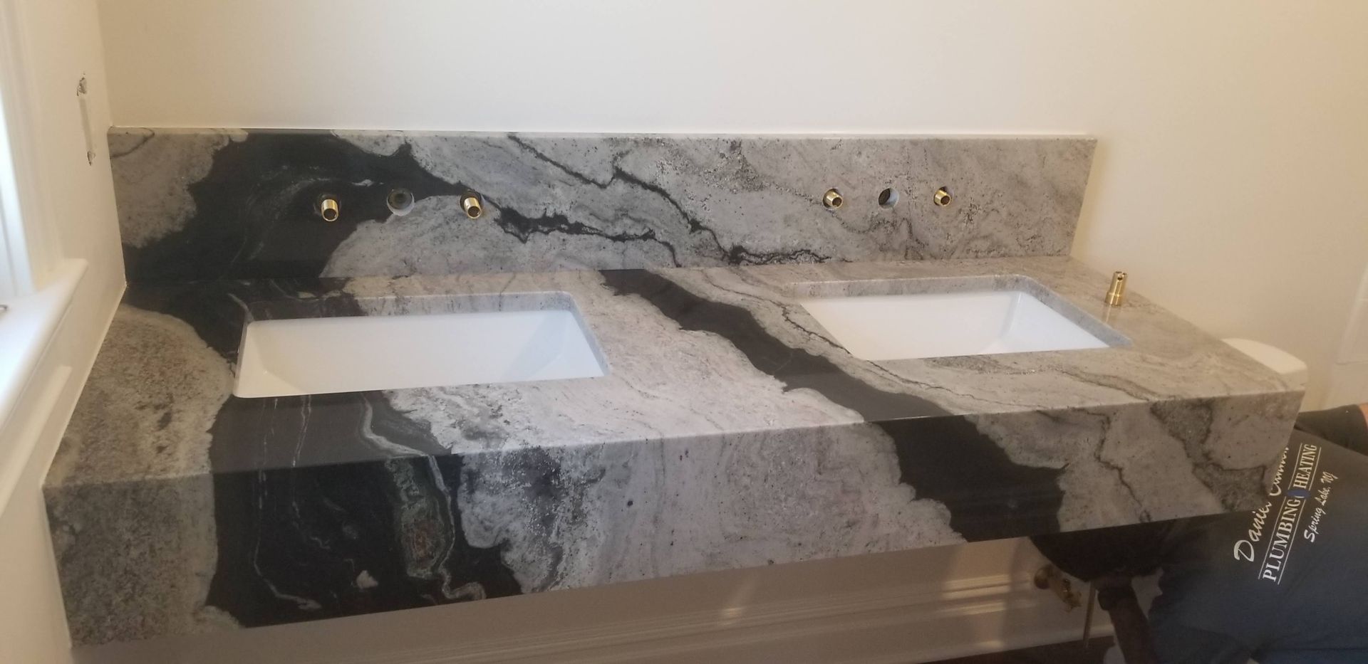 A double sink granite countertop in a bathroom. Dark veining against gray and white stone.