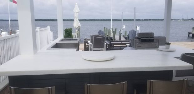 Outdoor bar with white counter, stainless steel sink, and water in the background.