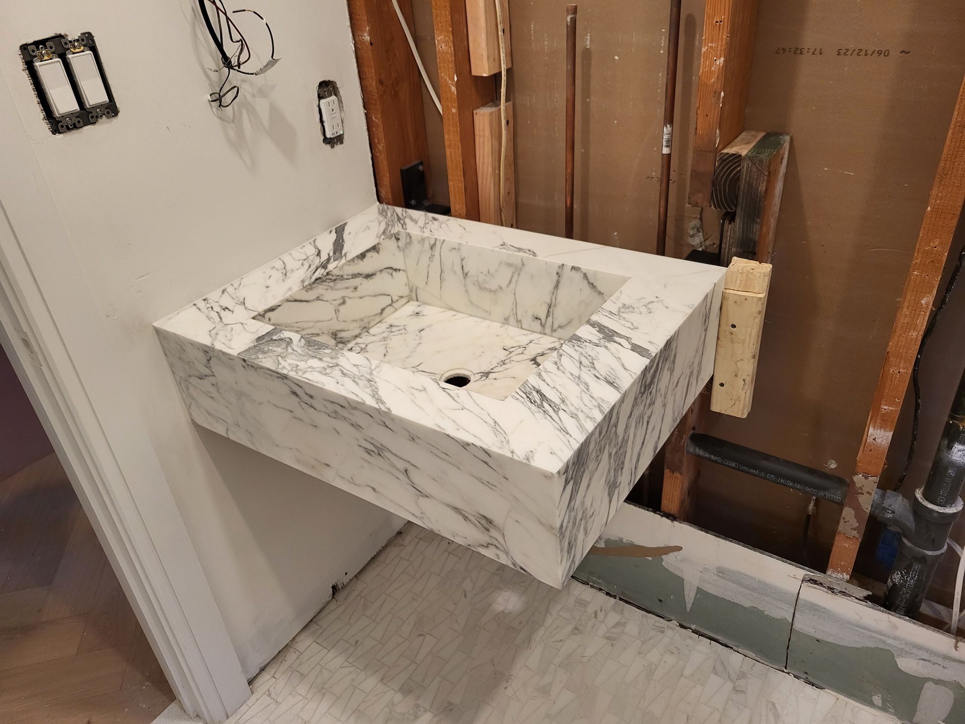 Marble wall-mounted bathroom sink in a room under construction, with exposed wall studs and wiring.