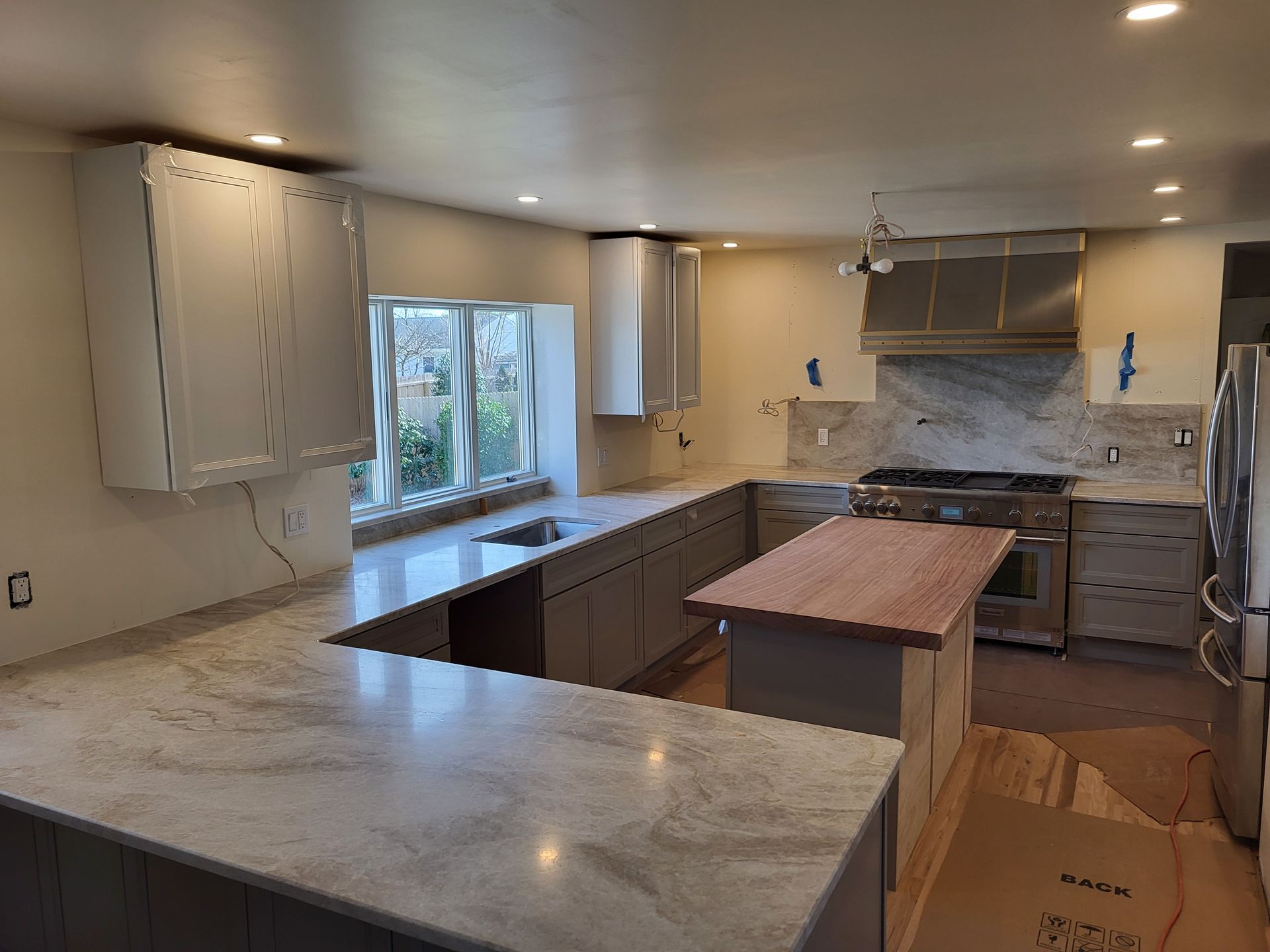 Newly renovated kitchen with gray cabinets, marble countertops, and a wood island countertop.