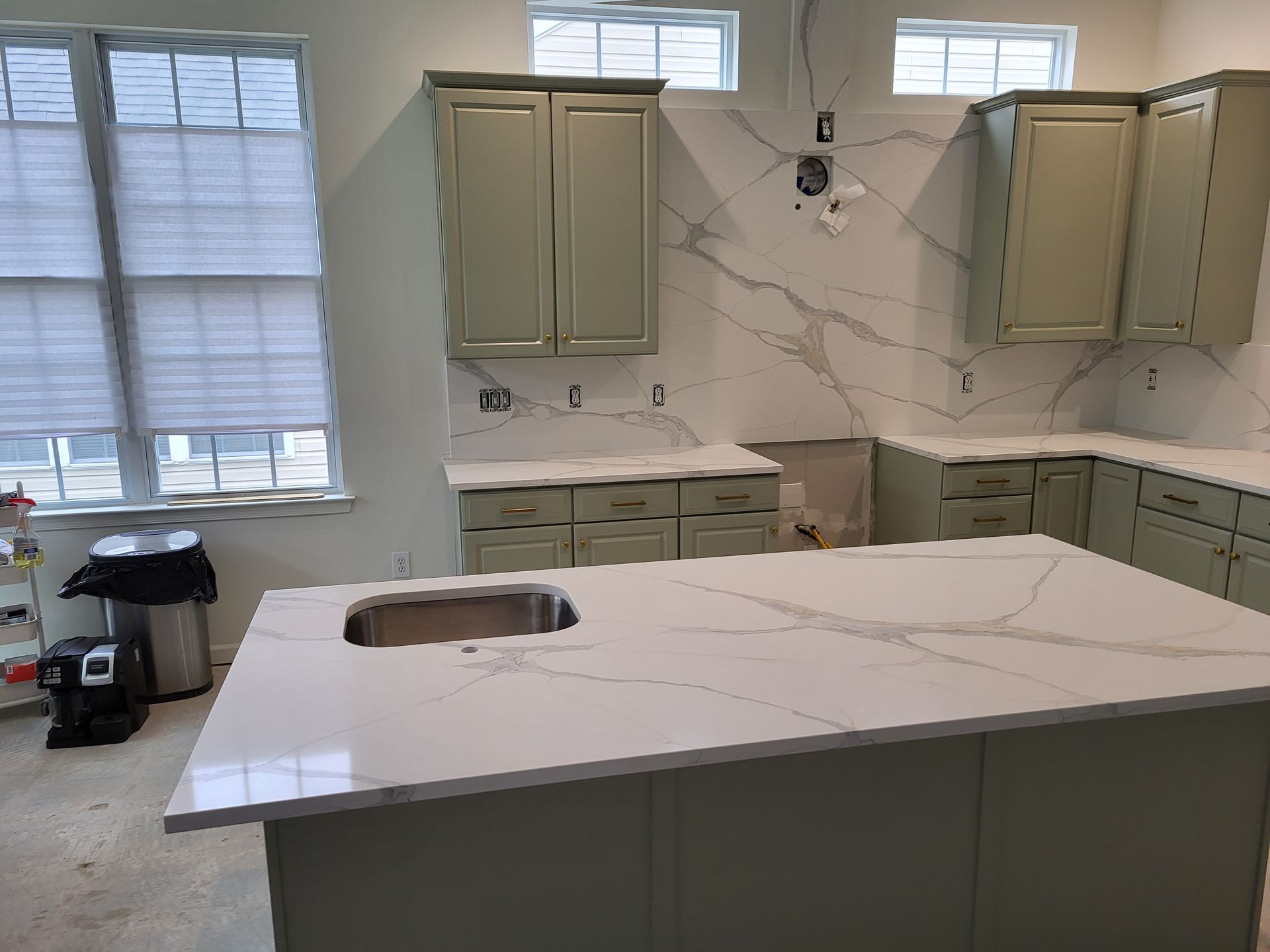 Kitchen remodel with sage green cabinets, white countertops, marble backsplash, and an island with a sink.