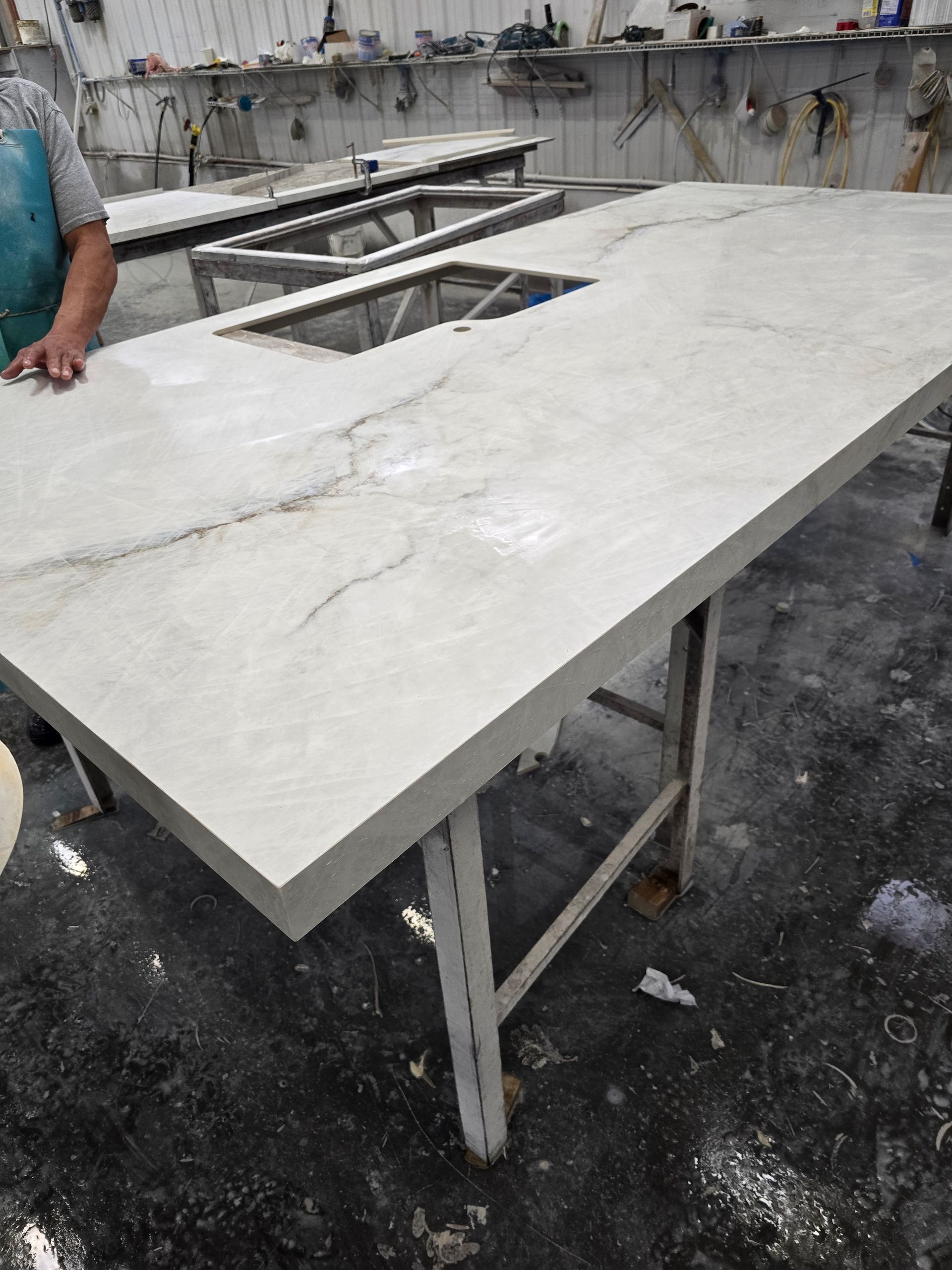 Large light-colored countertop with rectangular cutout, on metal supports. A person's hand is visible on the left.