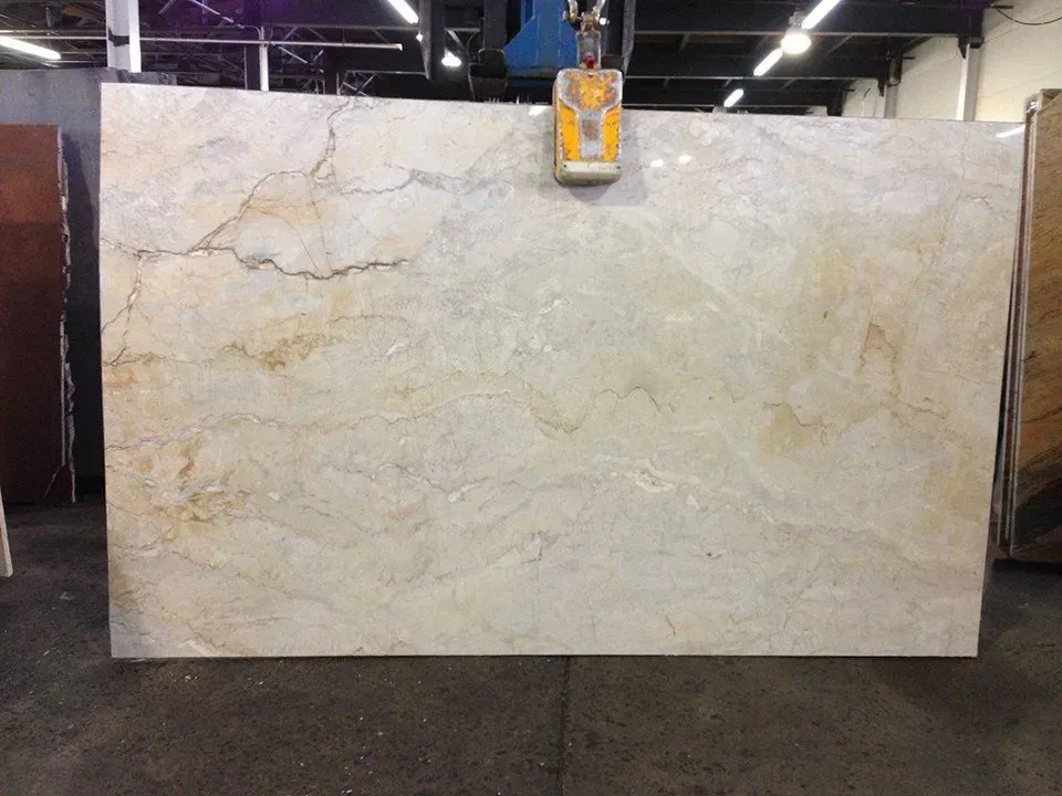 Large beige and tan marble slab suspended by a yellow lifting device in a warehouse.