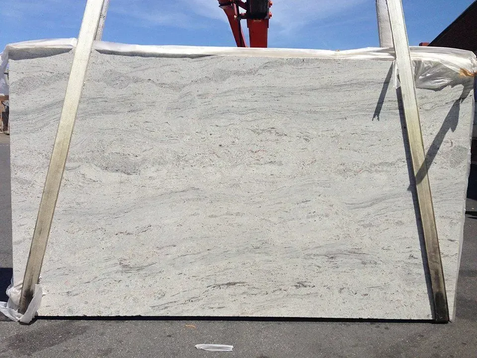 Large rectangular slab of white granite with gray and brown veining, being lifted by straps.