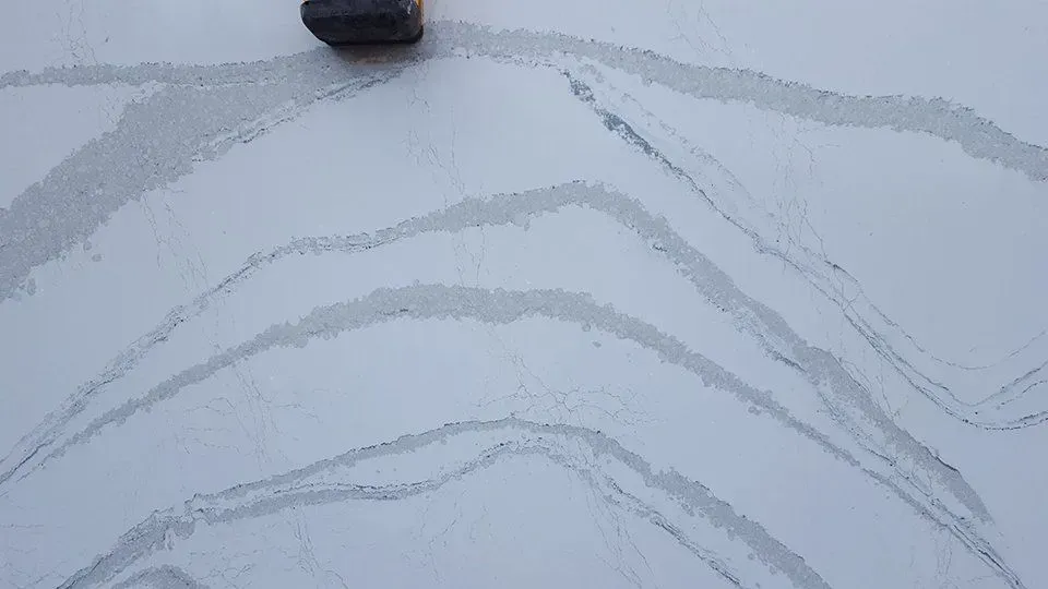 White surface with gray, wavy streaks, small rock in upper center.