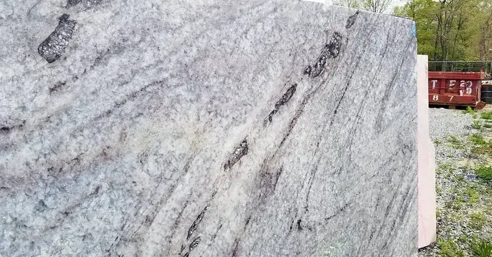 Gray and white granite slab with dark veining, outdoors near gravel and a red container.