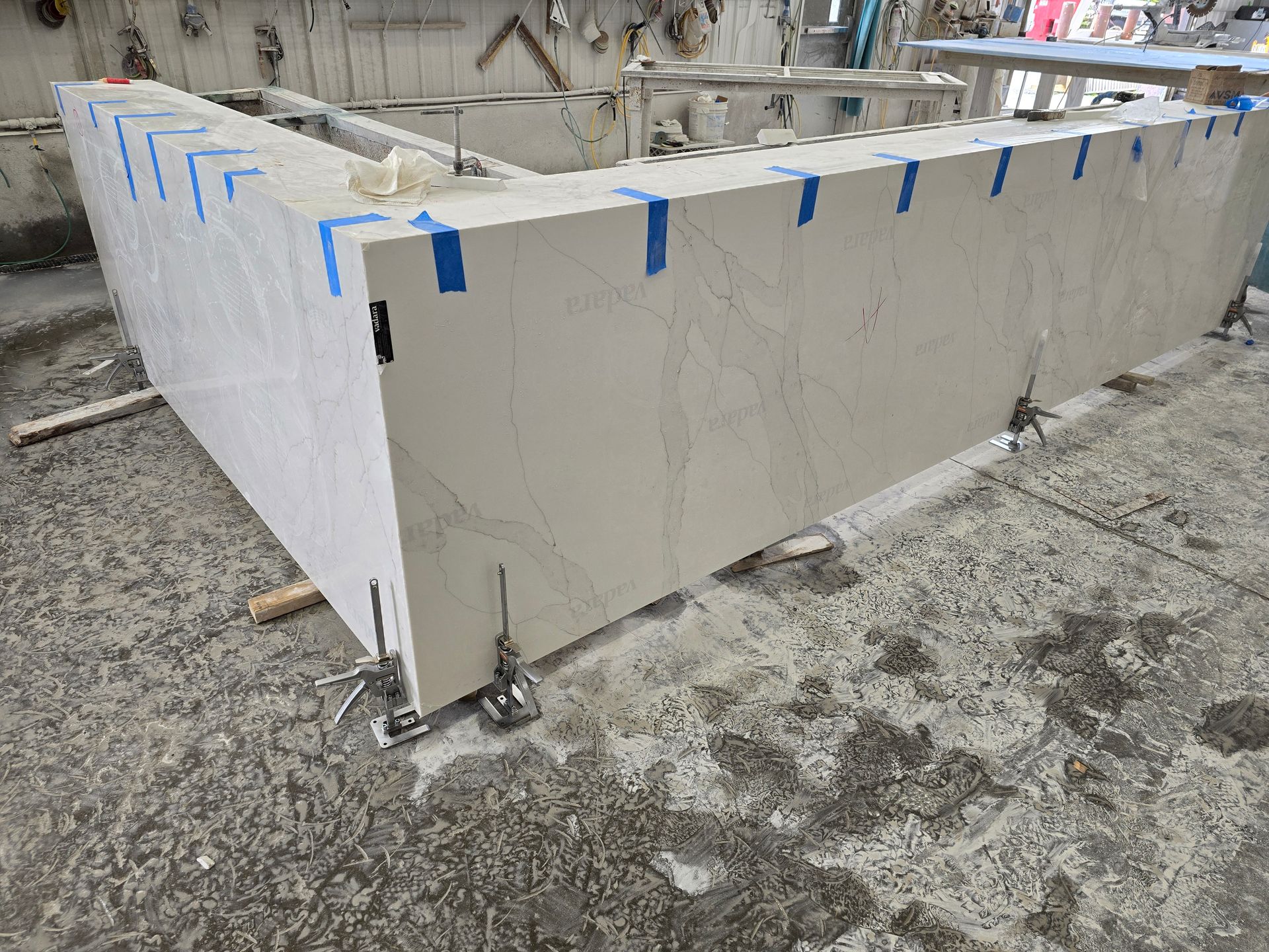 A large, light-colored countertop under construction; taped corners and clamps are visible.