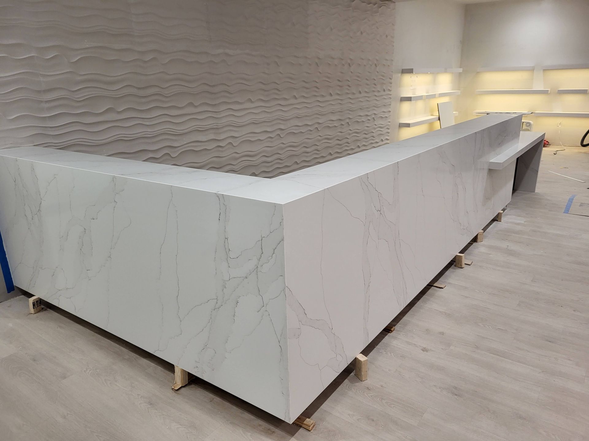L-shaped white quartz counter with gray veining in a room with textured white wall and recessed shelves.