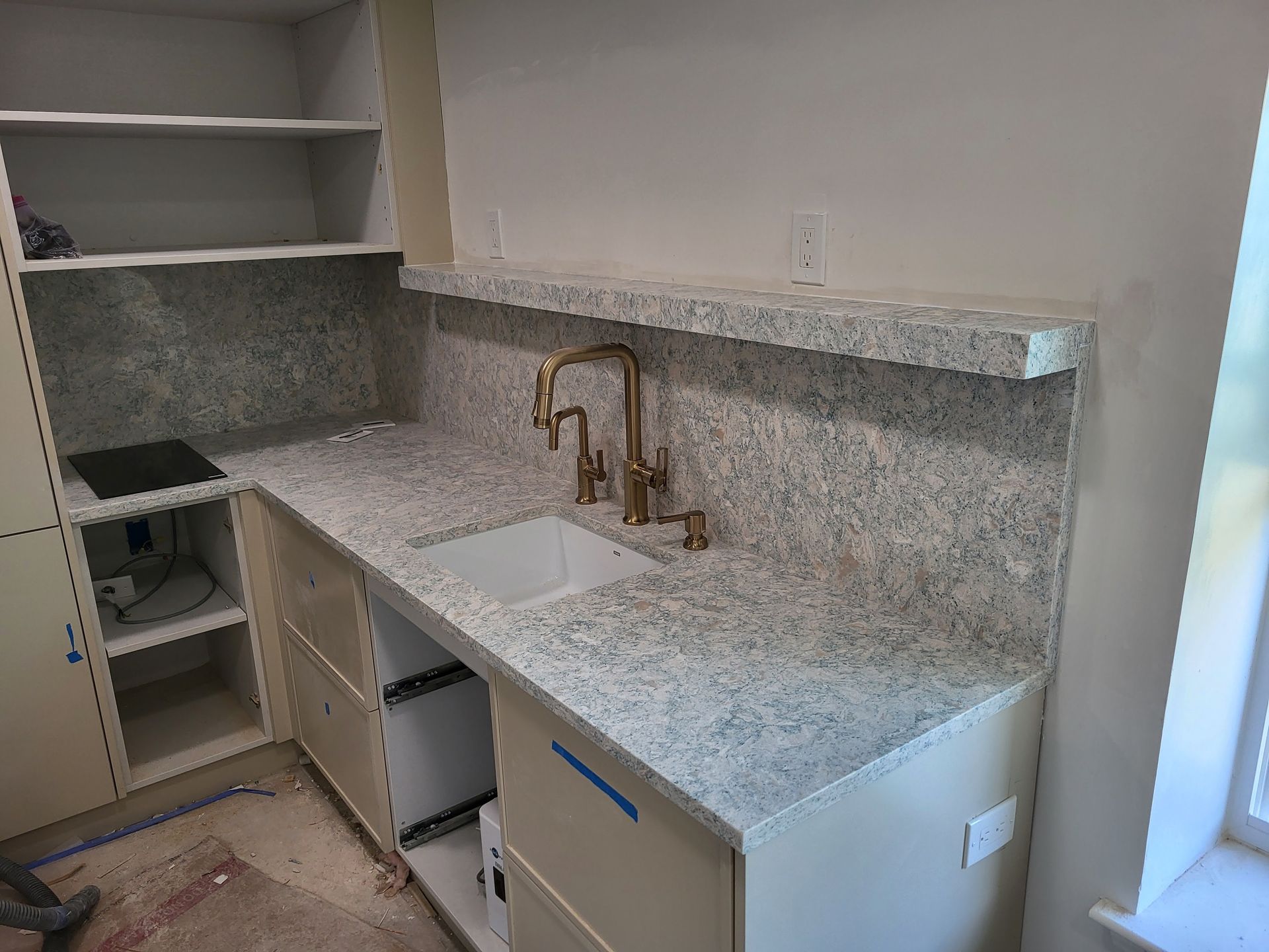 Kitchen area with white cabinets, light granite countertop, sink, and gold faucet.