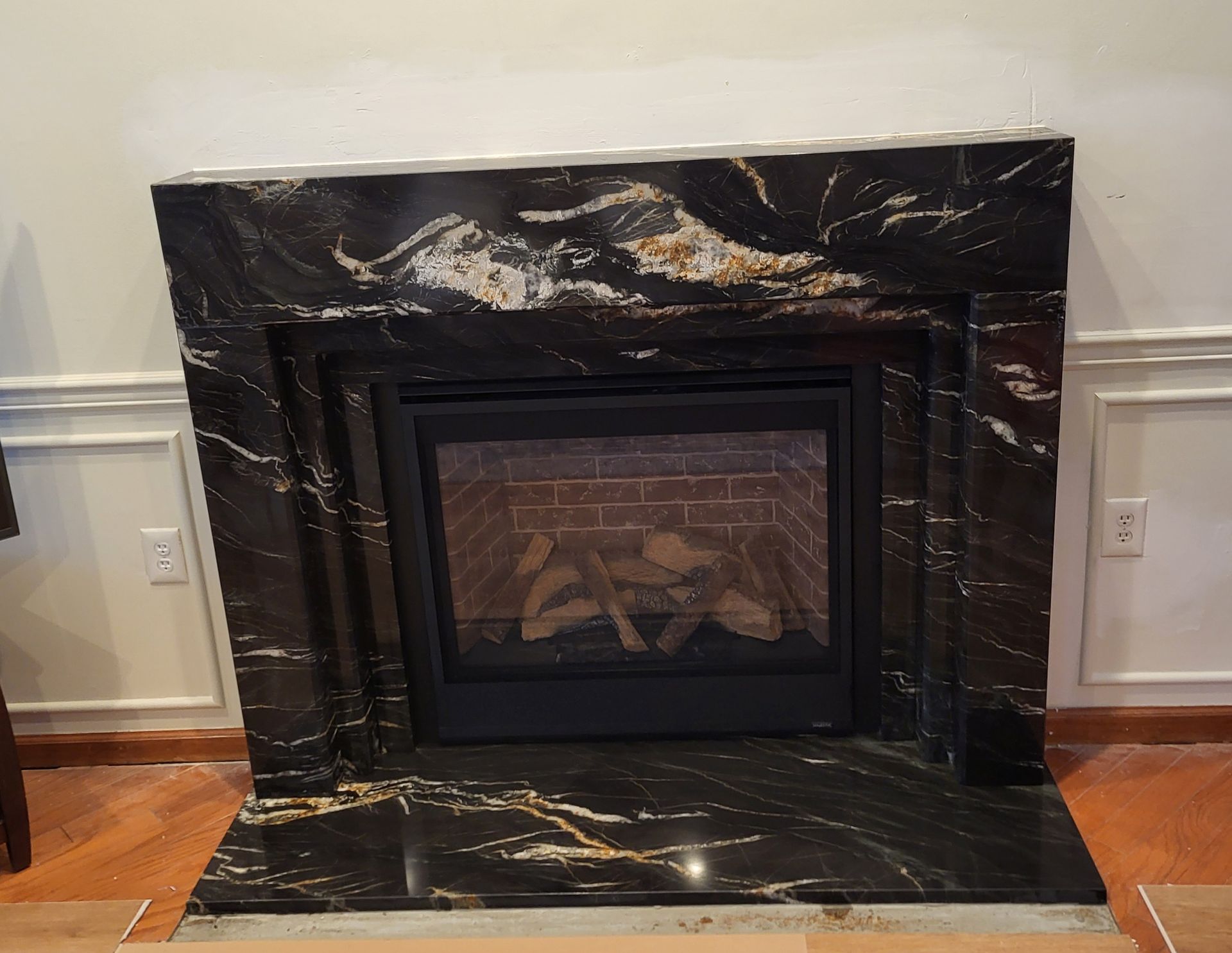 Black granite fireplace with gold veining, mounted on a wall with white trim and a brown floor.