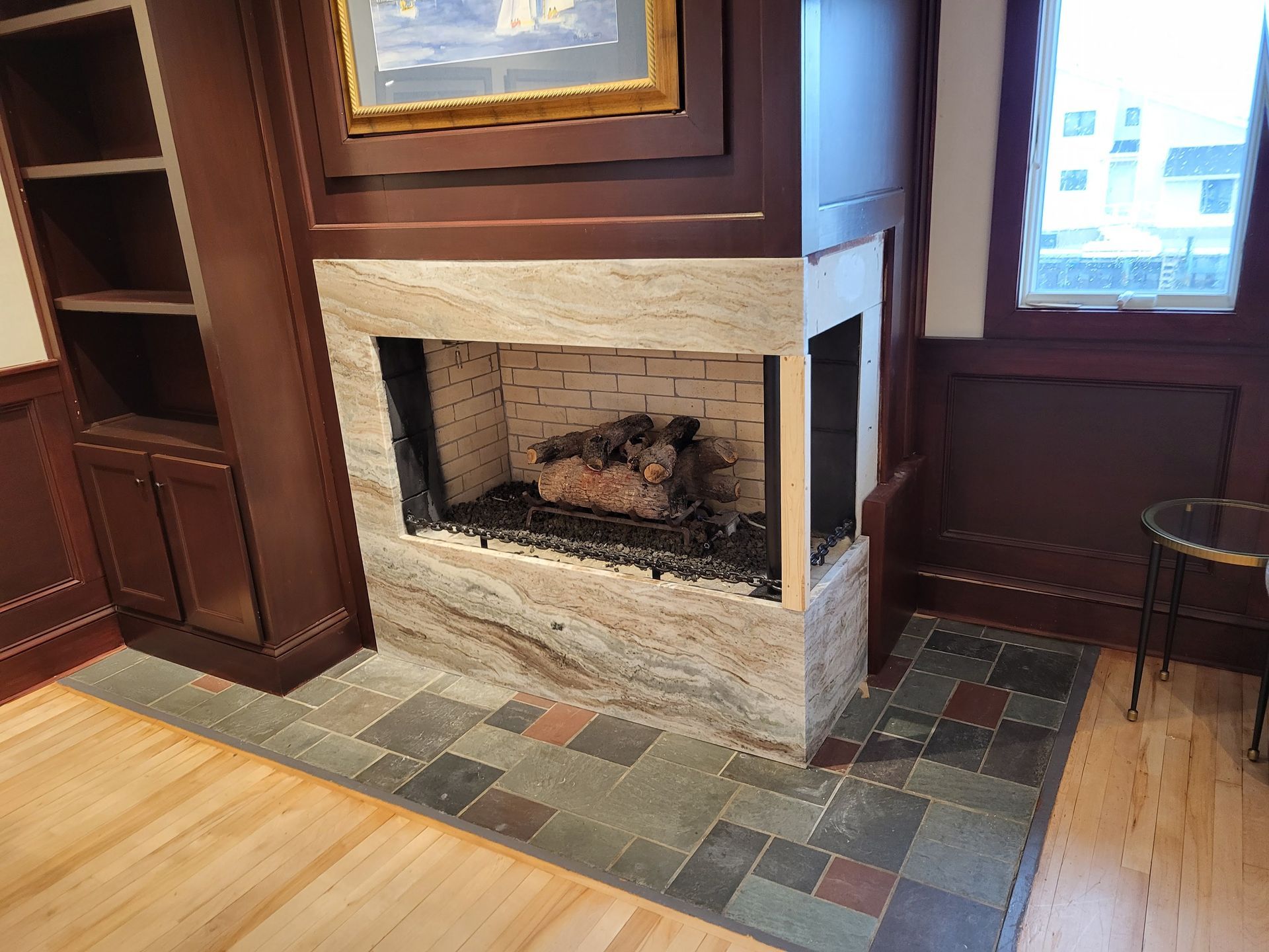Fireplace with stone surround, dark wood built-ins, slate tile hearth, hardwood floor, artwork, and small table.