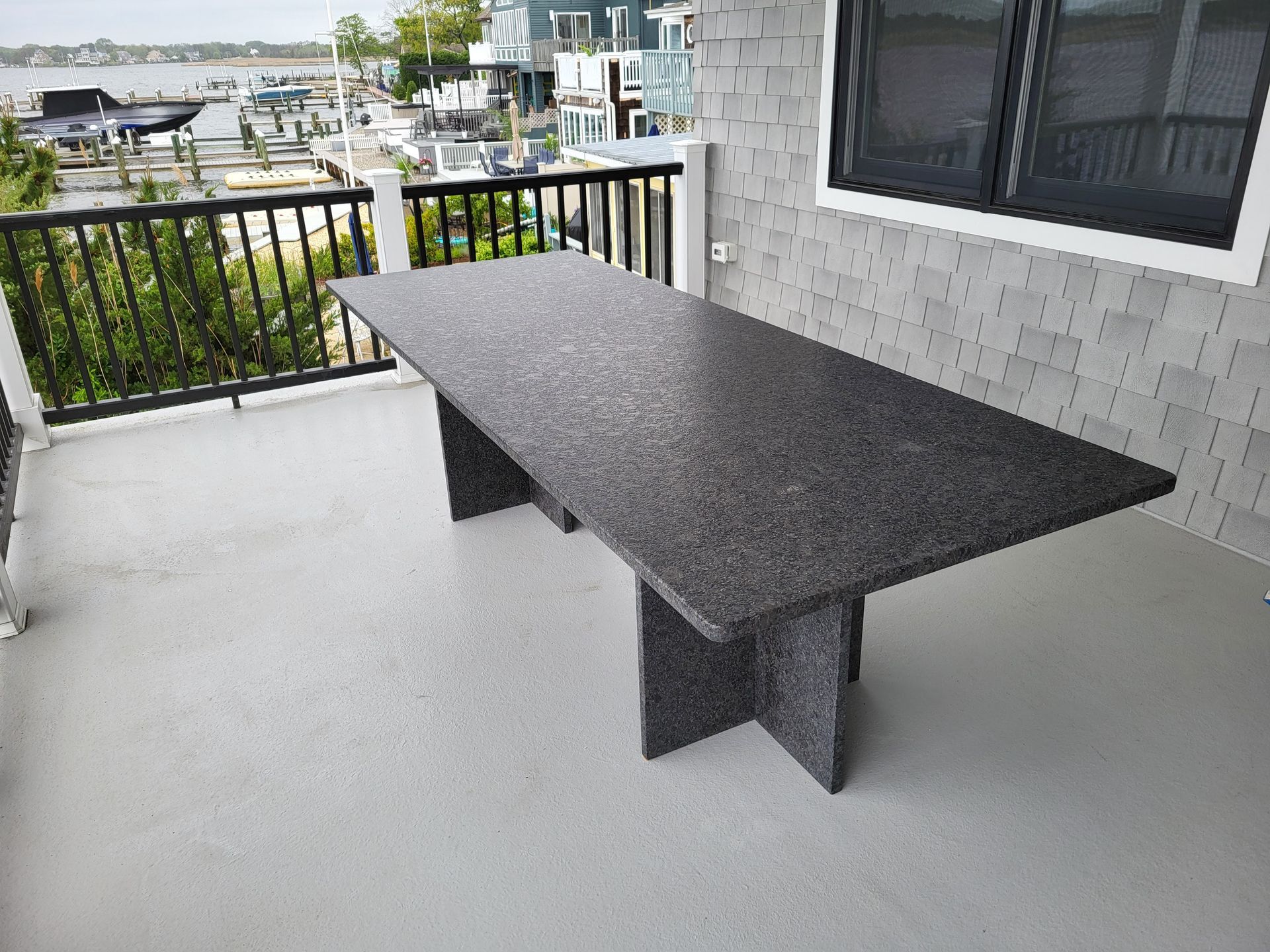 Large granite-topped outdoor dining table on a porch overlooking a harbor.