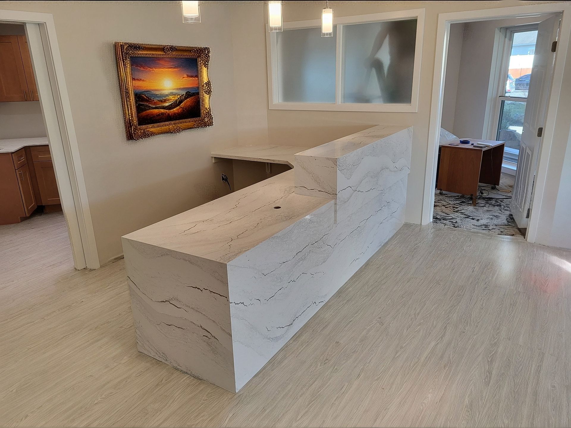 Reception desk with white marble-like finish, artwork, and light-colored flooring, near an open doorway.