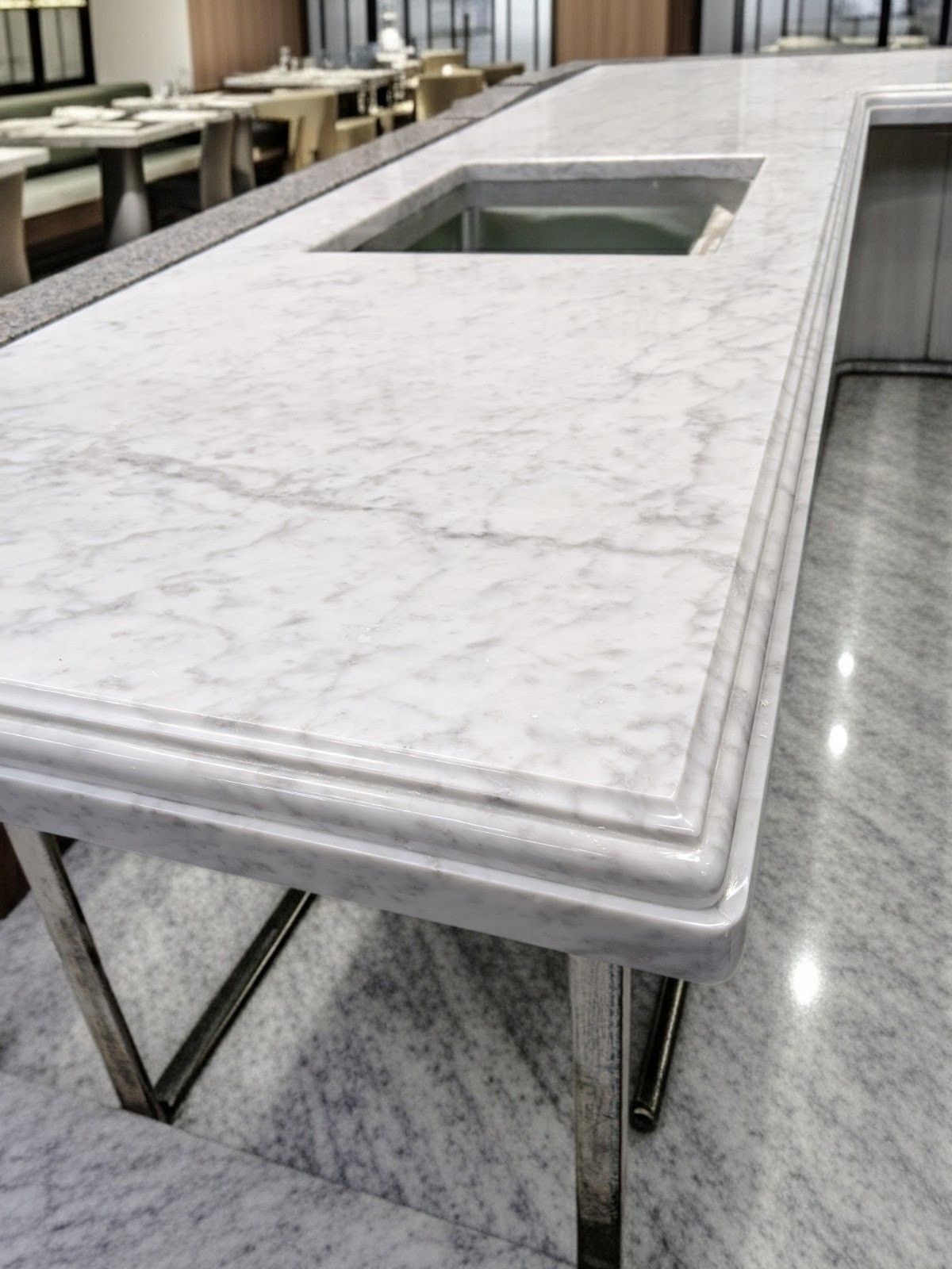 Marble countertop with built-in basin, stainless steel legs, in a modern dining setting.