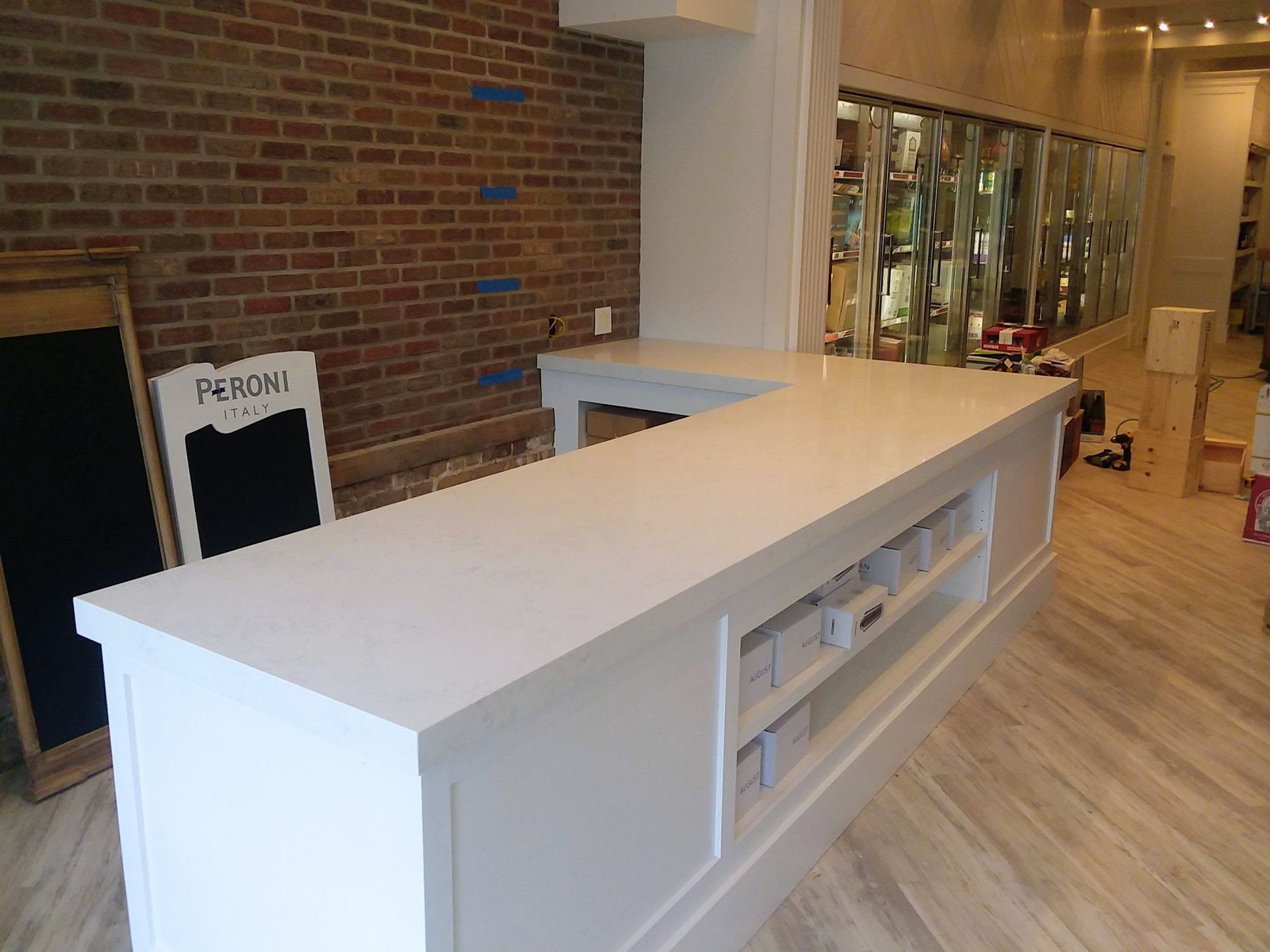 White countertop with cabinets and open shelves, facing a brick wall and store window.