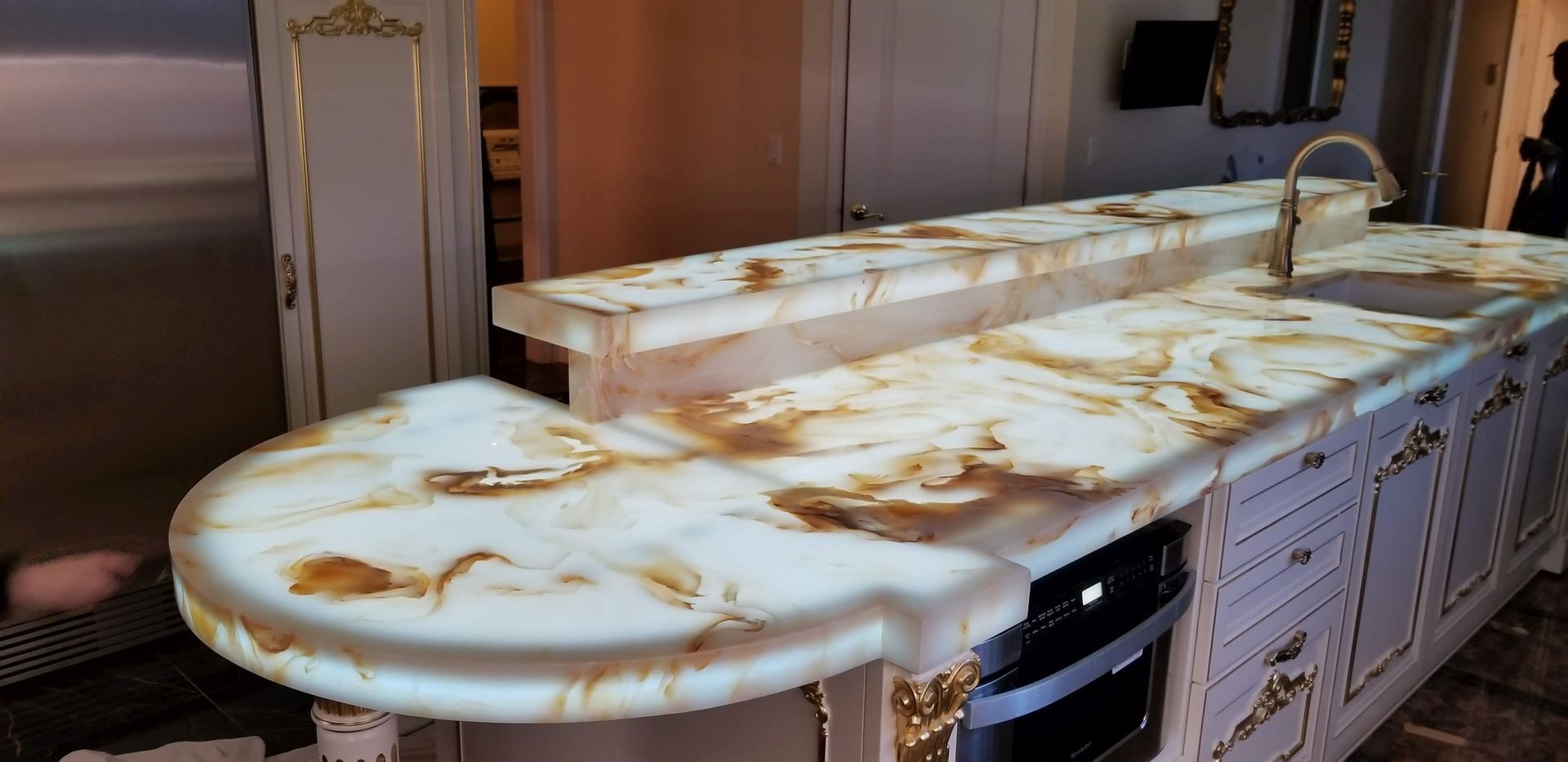 Kitchen with a backlit marble countertop and light-colored cabinetry with gold accents.