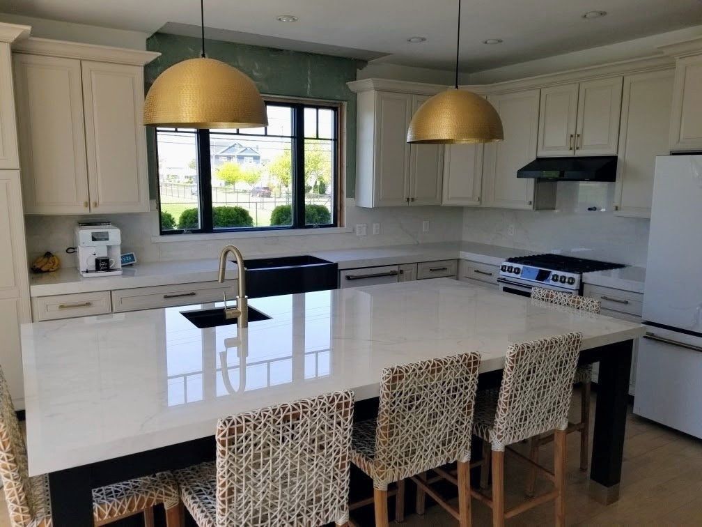 Kitchen with white cabinets, gold pendant lights, black sink, and island with woven bar stools.