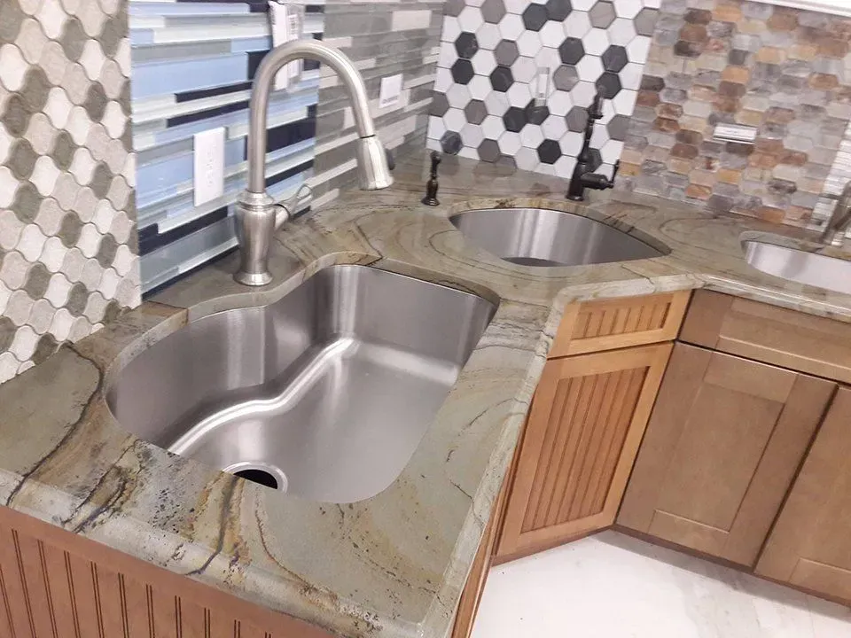 Kitchen corner with three stainless steel sinks and light brown cabinets under a patterned tile backsplash.