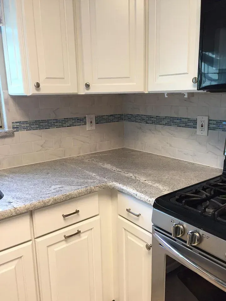 White kitchen cabinets with a gray countertop and blue-tiled backsplash. A gas range is visible on the right.