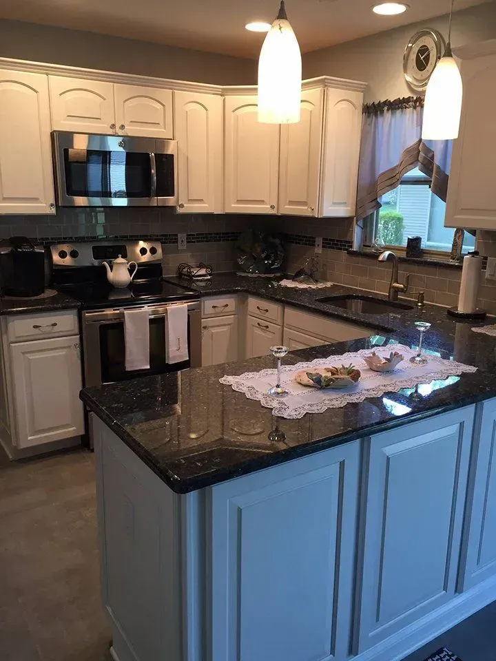 Kitchen with white cabinets, black countertops, stainless steel appliances, and a central island.
