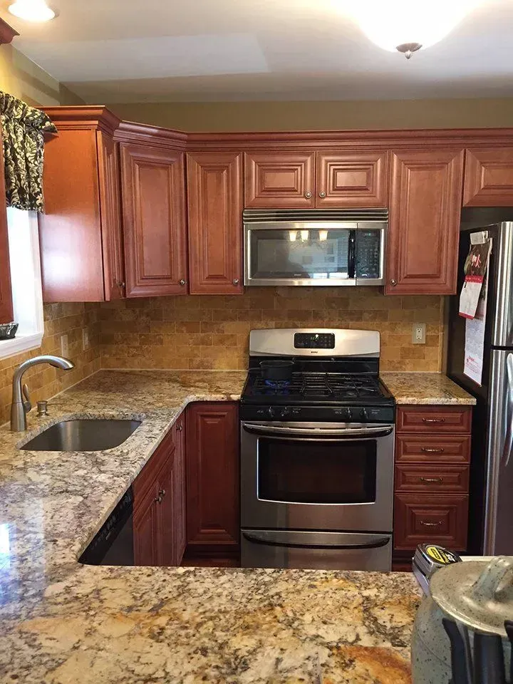 Kitchen with red-brown cabinets, stainless steel appliances, granite countertops, and a tiled backsplash.