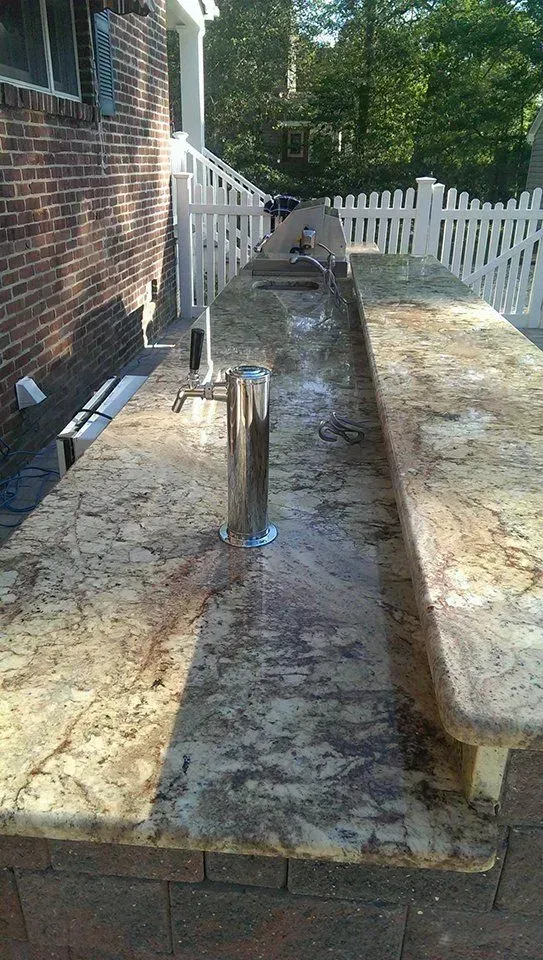 Outdoor granite countertop with sink and faucet, beside a brick wall and white picket fence.