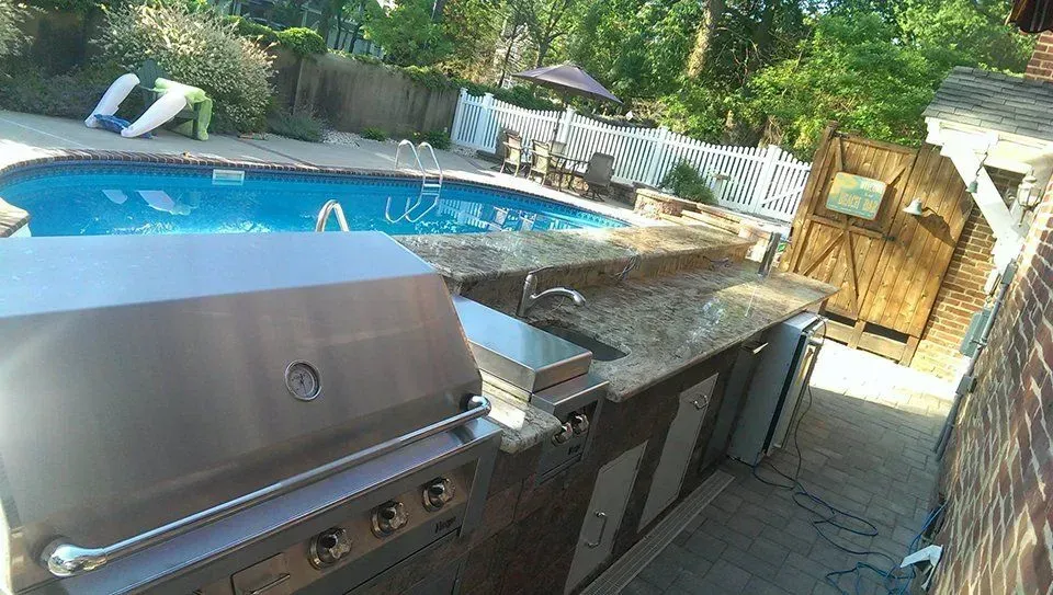 Outdoor kitchen with stainless steel grill, granite countertop, and pool in the background.