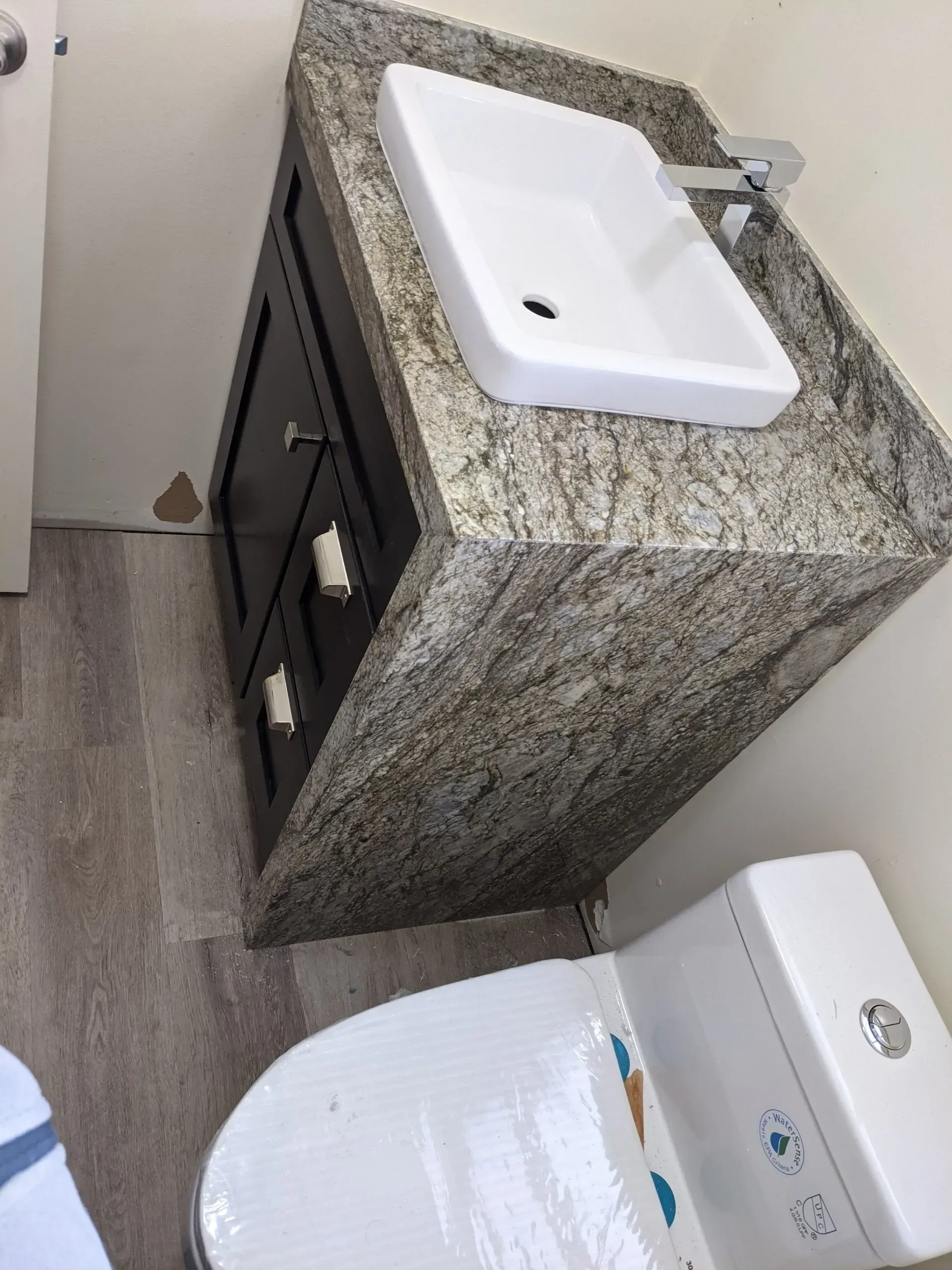 Bathroom vanity with granite countertop and rectangular sink next to a toilet.