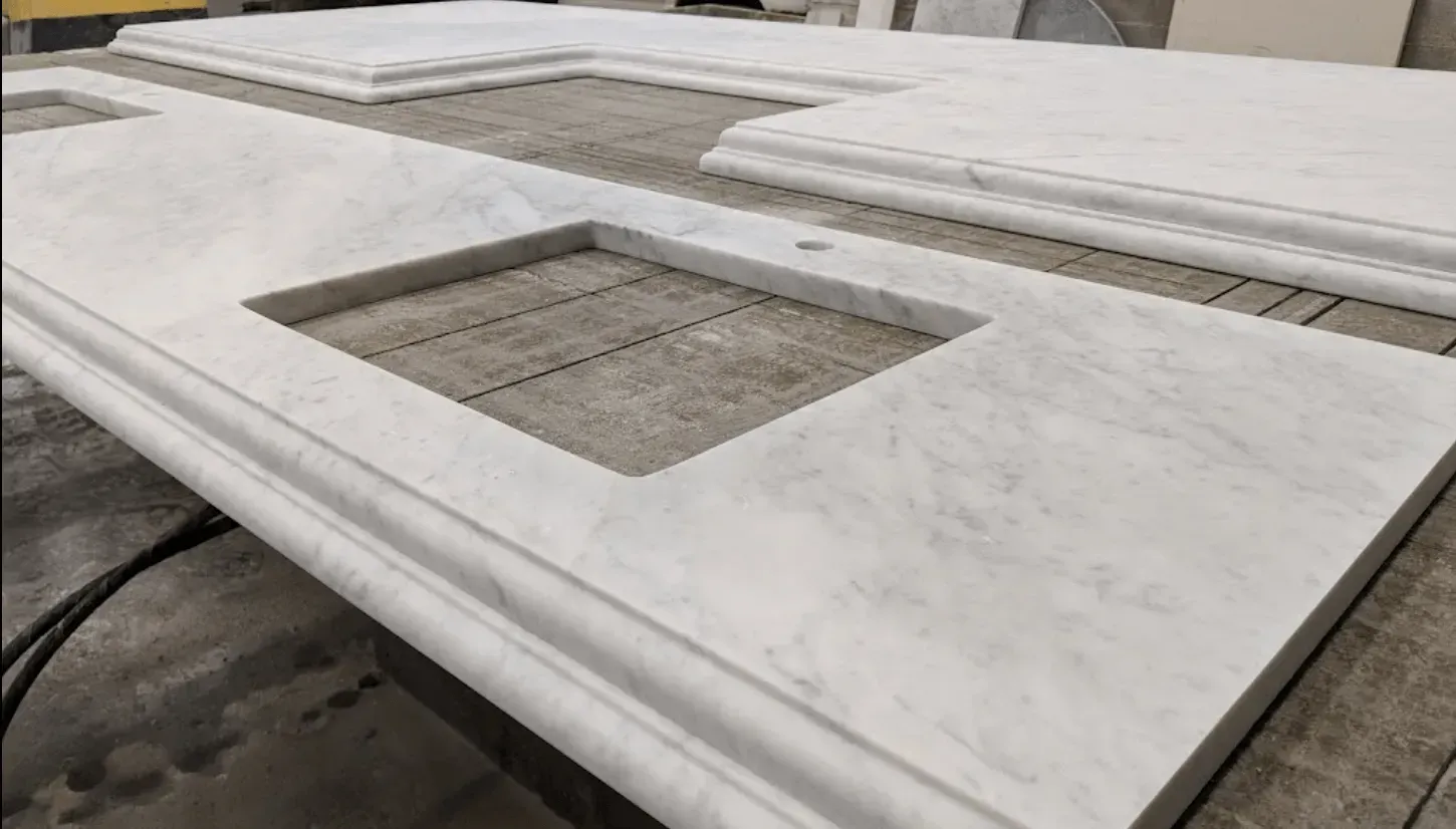 White marble countertops with a sink cut-out and rounded edges sit on a surface, likely in a workshop.